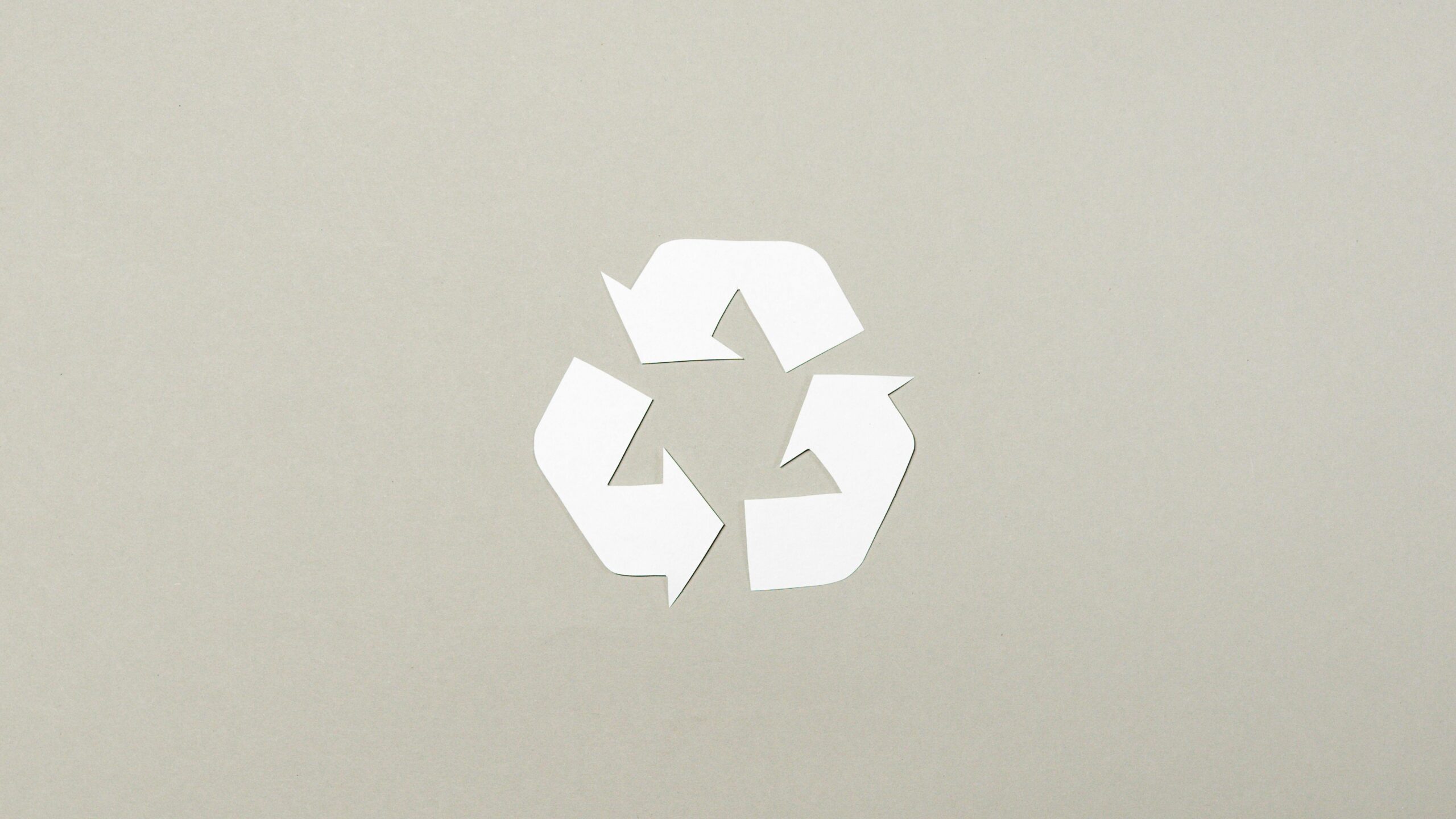Simple paper cutout recycle symbol on a neutral gray background, emphasizing sustainability.